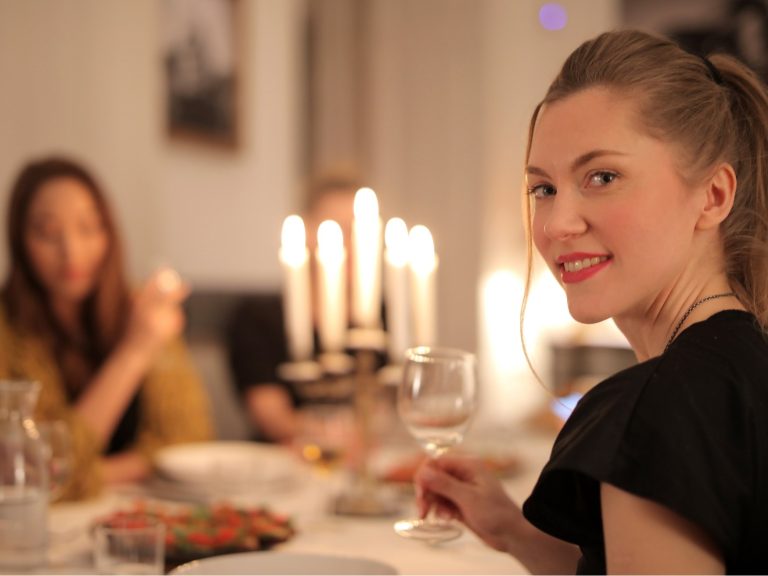 Kuva pöydästä, jolla on aseteltu astioita ja tarjoiluvalmisteluja valmiina. Henkilöt istuvat pöydän ääressä ja noudattavat pöytätapoja.